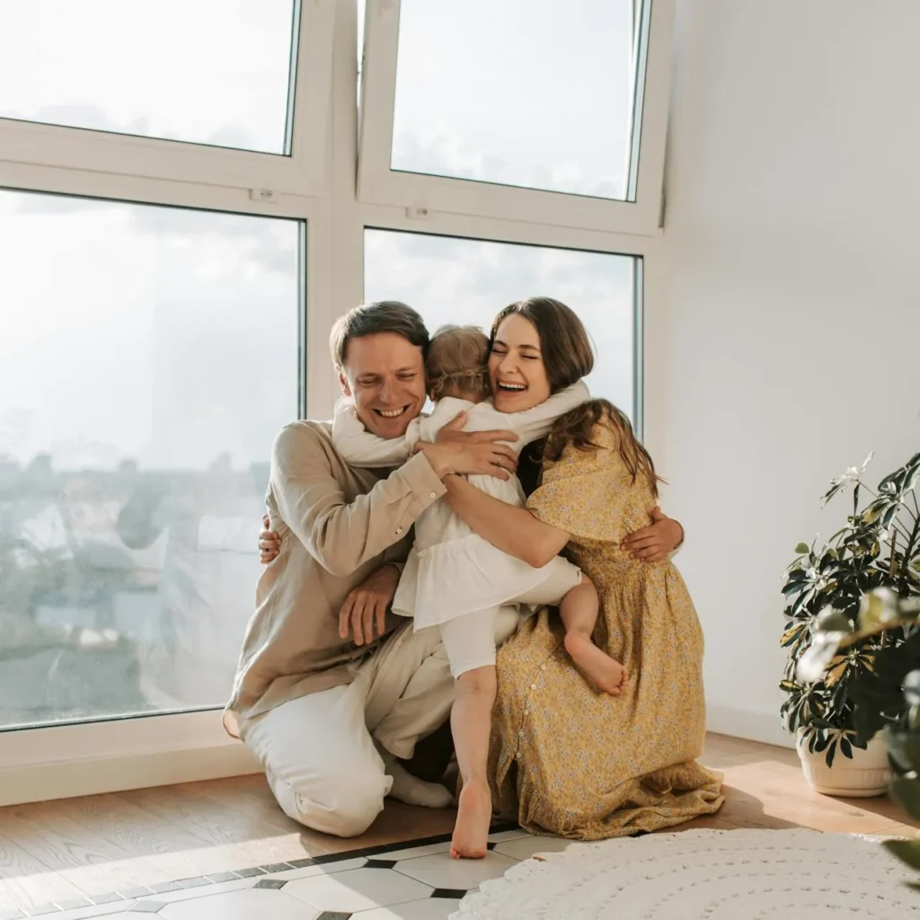 Smiling family of three embracing warmly in a sunny room.